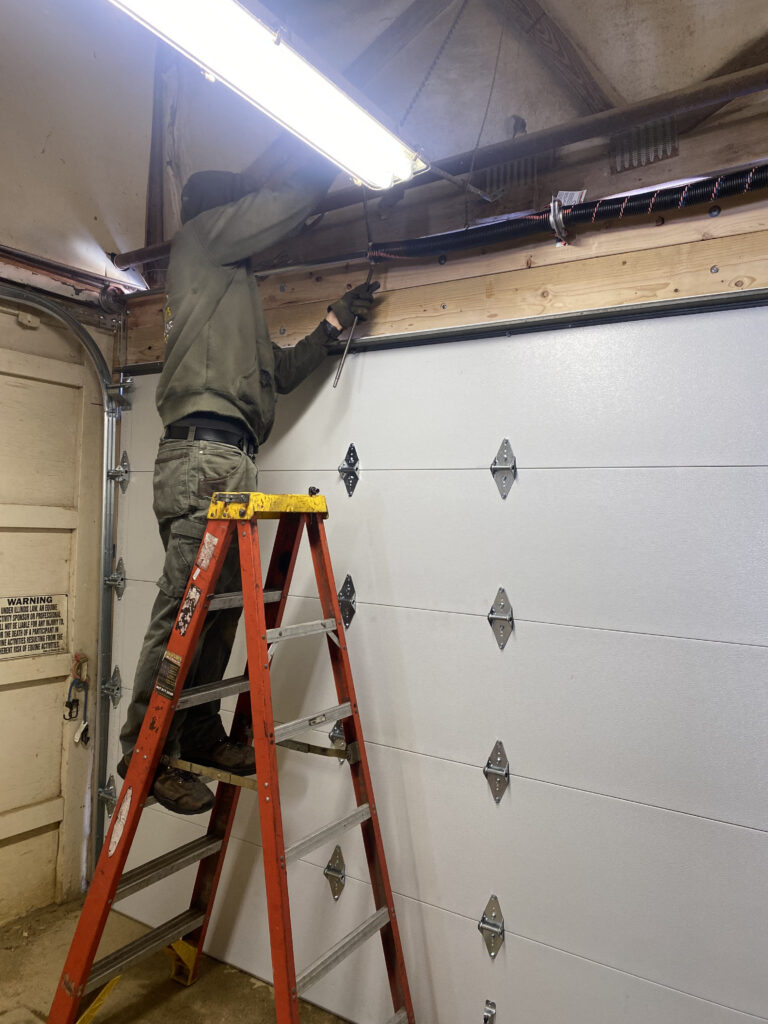 Garage door repair; man on ladder completing garage door spring repair